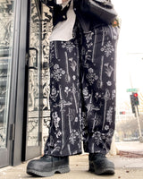 Close up of dark black pants with a print of vintage swords and flowers on loungewear bottoms on a city street in Wisconsin 