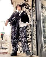 A plus size model wearing dark black pants with a print of vintage swords and flowers on loungewear bottoms in a city street.